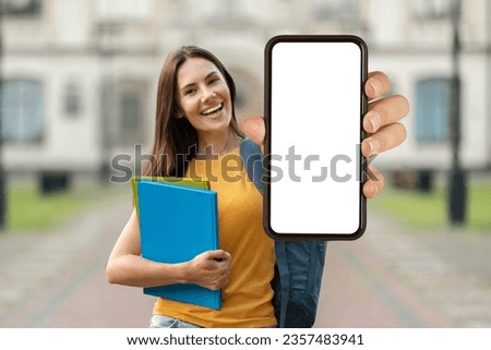 Educational Offer. Beautiful Smiling Female Student Demonstrating Blank Smartphone With Empty Screen At Camera While Standing Outdoors, Happy Young Woman Recommending New Study App, Mockup Royalty-Free Stock Photo #2357483941