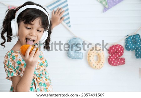 Little girl holds a rope with the numbers 2024 on it and enjoys half an orange in her hand, number 2024 made from beautifully printed fabric 