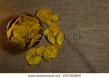 Crispy banana chips in a bowl , dried banana chips or banana waffers spilled out from wooden basket, kerala chips is a snack item side view top view, banana chips is also known as upperi.
