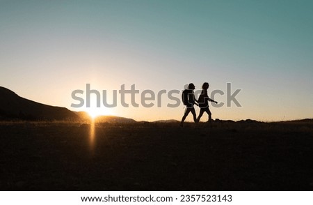 silhouette of two girls with backpacks while traveling in the mountains at sunset. two people walk along the mountain range at sunset. travel with freedom.