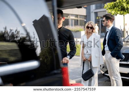 Business couple standing by a minivan taxi waiting for their chauffeur or porter to help them with a suitcases. Concept of business trips and travel Royalty-Free Stock Photo #2357547559