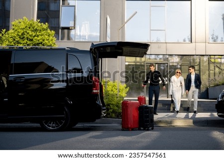 Driver or concierge helps a business couple carry their suitcases to minivan taxi from hotel. Concept of business travel and transportation service Royalty-Free Stock Photo #2357547561