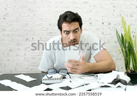 Close up of unhappy man sitting at the table, stressed and confused by calculate expense from invoice or bills, have no money to pay mortgage or loan. High prices and spending money concept Royalty-Free Stock Photo #2357558519