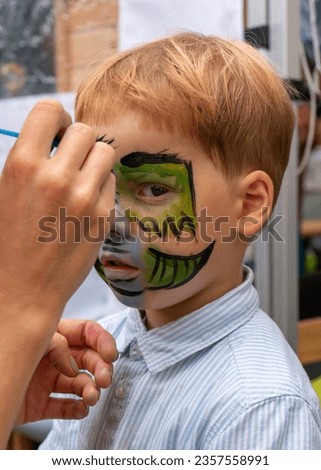 The face of a little boy with a pattern on his face. The artist draws a picture of a kind, green dragon on the face of a child 