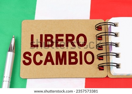 Economy and finance concept. On the flag of Italy lies a pen and a notebook with the inscription - free trade. Text in Italian.