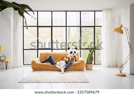 Unrecognizable female couple lying on sofa giant panda bear and sloth stuffed animal masks indoor. Girls in costume posing funny studio photo with natural light and window in background. Copy space.