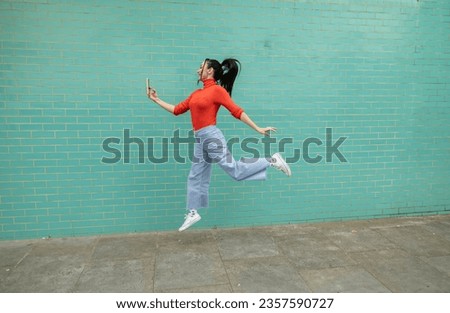 pretty woman jumping and making selfie light blue wall background