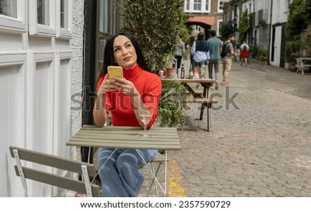 pretty tourist woman on outdoor restaurant terrace looking at her smart phone and drinking a glass of wine