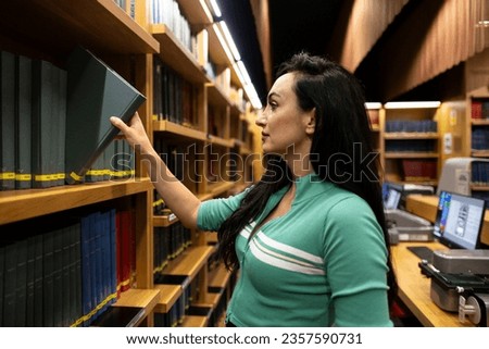 young woman in a library picking up a book Royalty-Free Stock Photo #2357590731