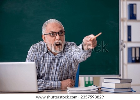 Old male teacher sitting in front of green board Royalty-Free Stock Photo #2357593829
