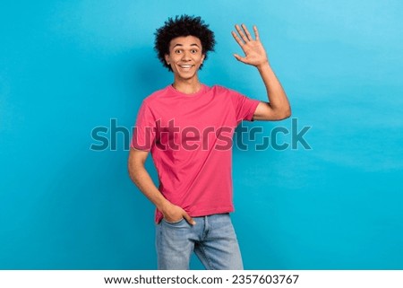 Portrait of good mood friendly guy dressed stylish t-shirt waving palm say hello hold hand in pocket isolated on blue color background