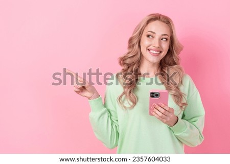 Photo of young girl pointing finger empty space recommend shopping website amazon offer ad hold iphone isolated on pink color background