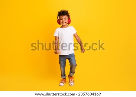 Full length photo of funky cheerful little boy dressed white t-shirt walking enjoying songs earphones isolated yellow color background