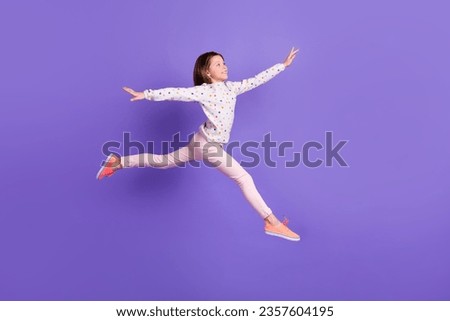 Full length photo of excited carefree little girl dressed dotted pullover running jumping high isolated purple color background