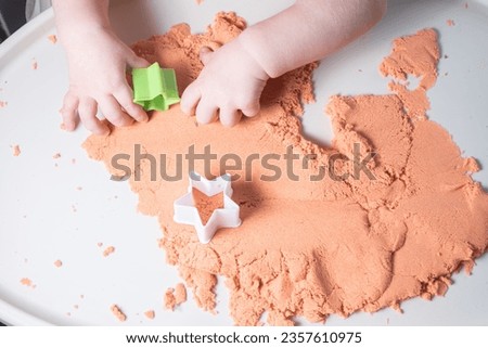  Faceless baby is playing with kinetic sand. Child handles with a toy in the shape of a star. Royalty-Free Stock Photo #2357610975