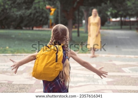 A happy schoolgirl, carrying her schoolbag, joyfully embraces her loving mother in a city park. This playful daughter's after-school reunion underscores their strong family connections.  Royalty-Free Stock Photo #2357616341