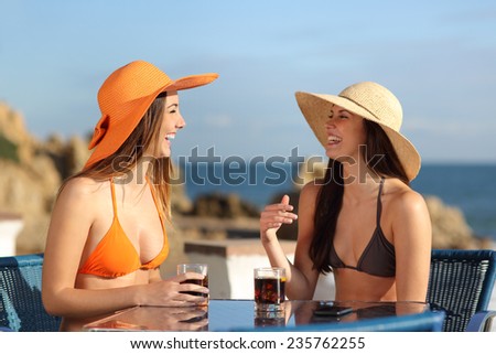 Two friends talking in an hotel terrace on holidays with the beach in the background