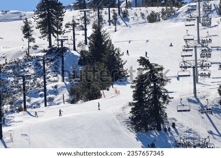 View of snowed mountain slopes with people skiing, snowboarding and chair lifts. Ski resort.
