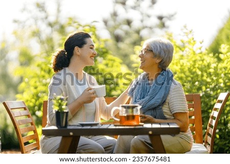 Happy young woman and her mother drinking tea in summer morning. Family sitting in the garden with cups and enjoying the conversation. Royalty-Free Stock Photo #2357675481
