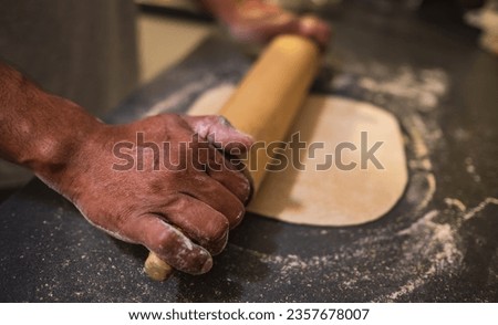 Man rolling out dough on kitchen table. Baking concept. Hands roll dough on black background. Baker cooking pastry. Kneading, Closeup of dough being flattened. Chef rolling out dough in kitchen