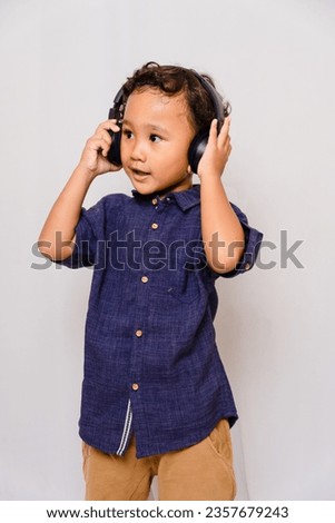 A cute boy in a blue shirt is listening to music with headphones. grey background. acting like a Disk Jockey.