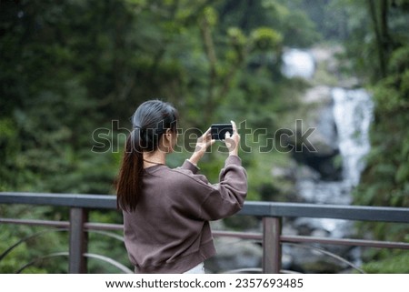 Woman use mobile phone to take photo on waterfall