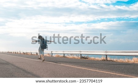 Rear view of young woman traveler with backpack walking on street road. Life balance with freedom travel lifestyles. Minimal style with blue sky and copy space. Royalty-Free Stock Photo #2357704119