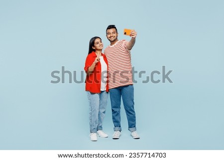 Full body smiling young couple two friends family Indian man woman wear red casual clothes t-shirts together do selfie shot mobile cell phone post photo show v-sign isolated on plain blue background