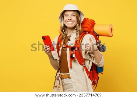 Young woman carry backpack with stuff mat use mobile cell phone show thumb up isolated on plain yellow background Tourist leads active lifestyle walk on spare time Hiking trek rest travel trip concept Royalty-Free Stock Photo #2357714789