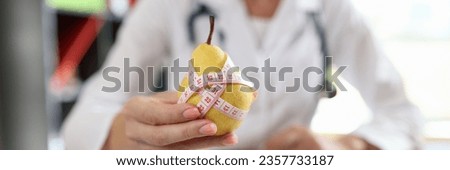 Close-up of doctor nutritionist holding ripe yellow pear with measuring tape. Healthy food, diet, vitamins and balanced nutrition concept
