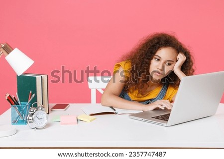 Boring young african american girl employee in office sit at desk work on laptop pc computer isolated on pink background. Achievement business career. Education in school university college concept