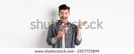 Excited man celebrating birthday, looking happy at bday cake with candle, making wish, standing happy against white background.