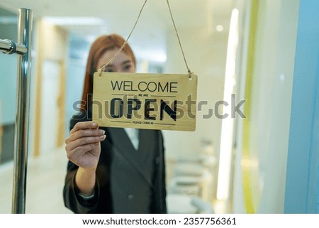 Woman hanging open sign on door, Store owner turning open sign broad through the door glass and ready to service.