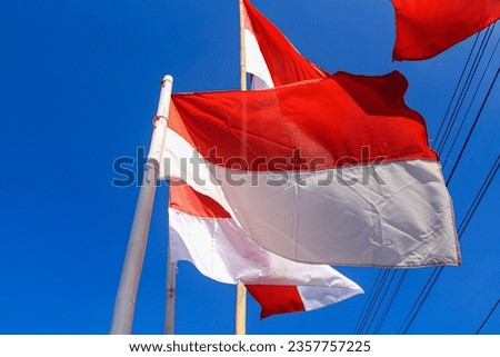 The Indonesian flag flutters against a bright blue sky in the background