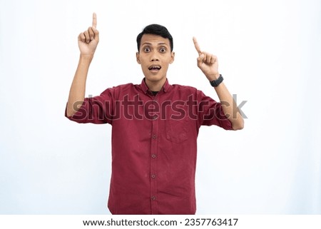 Asian man, businessman or student concept wearing red casual shirt pointing up at the copy space with a happy or surprised look on his face. Isolated white background.