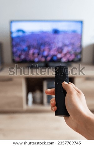 A woman's hand holds a TV remote control. Selective focus, noise. Shot point of view. Rest after a working day, watching a movie, vertical photo