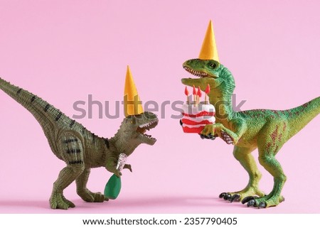 Cute plastic toys  green dinosaurs in party hats with cake and champagne bottle on pink background.