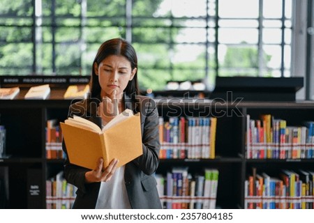 Asian woman thinking while reading a book.  She is researching in the library. Royalty-Free Stock Photo #2357804185