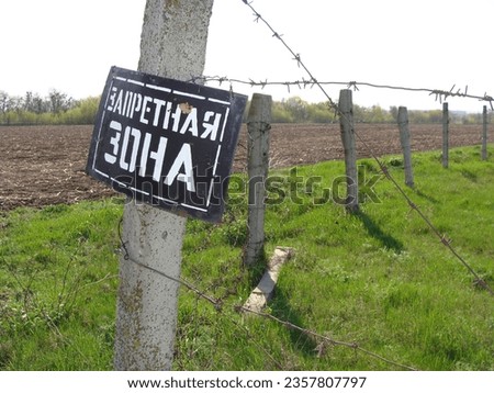 A sign with a prohibition inscription on a concrete pole with barbed wire. Text translation from rus: restricted area.