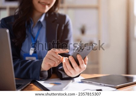 Close-up image of a beautiful young Asian businesswoman or female office worker is checking SMS or sending messages to someone on her smartphone while sitting at her desk in the office.