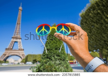 Symbol of peace. Multicolored glasses in the shape of a peace symbol in a hand on the background of the Eiffel Tower. The most important thing in the world is life without war.