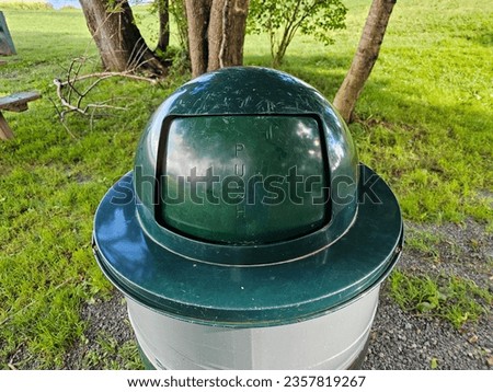 A closeup of a garbage can sitting in a park area.