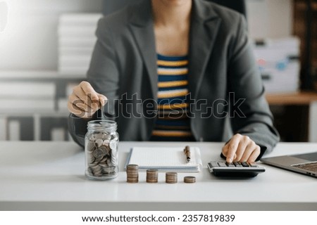 businesswoman holding coins putting in glass with using smartphone and calculator to calculate concept saving money for finance accounting in office