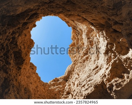 Golden yellow cave, with steep cliff and round hole on the top, with the blue sky view. Beautiful "Praia do Amado" beach near the Portimão town, Algarve. Coast of Atlantic Ocean in Portugal.