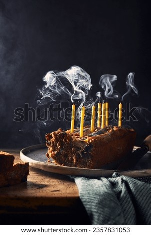 Sliced banana bread on a rustic wooden table and black background. It has birthday candles in it that are still smoking. Napkin on the table. Vertical still life picture. Space for copy.
