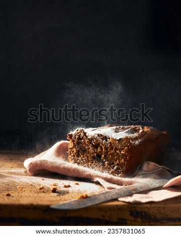 Sliced banana bread on a rustic wooden table and black background. Bit of sugar powder in the air creating motion in the picture. Vertical still life picture. Space for copy.