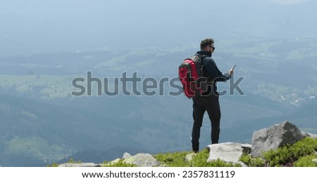 A traveler on top of a mountain is talking on the phone, taking pictures and having a video chat. Concept of communication in remote places of the world.