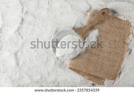 Pile of integral barley flour in wooden spoon and jute, linen sack  background and texture, top view  Royalty-Free Stock Photo #2357854339