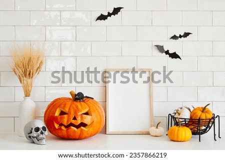 Halloween holiday concept. Empty photo frame, carved pumpkin jack-o-lantern, skull, bats on white brick  wall background