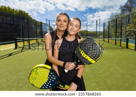 Two padel tennis players with rackets. Woman and girl teenager athlete with paddle racket on court outdoors. Sport concept. Download a high quality photo for the design of a sports app or web site.